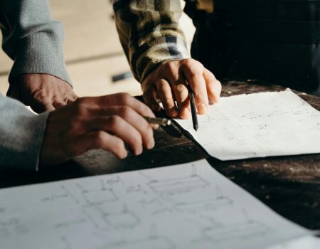 pexels-photo-7484159-7484159 Close-up of hands working on blueprints in a workshop environment.